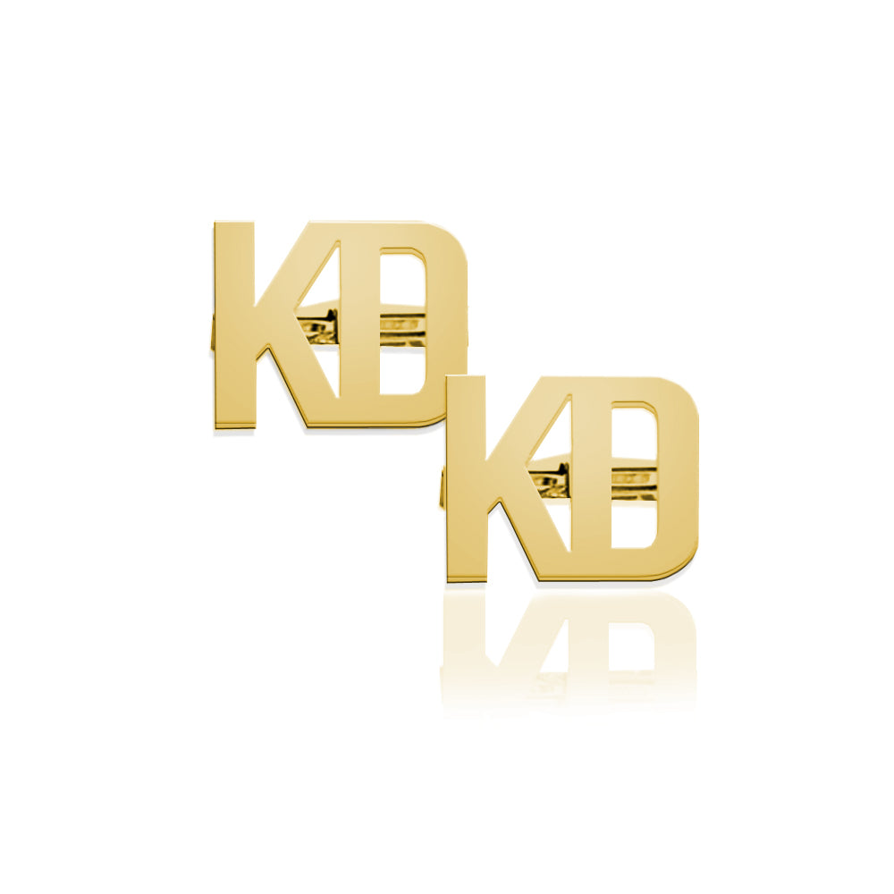 A pair of gold initial cufflinks featuring the letters 'KD' in a bold, blocky font, displayed on a clean white background with a soft reflection underneath.